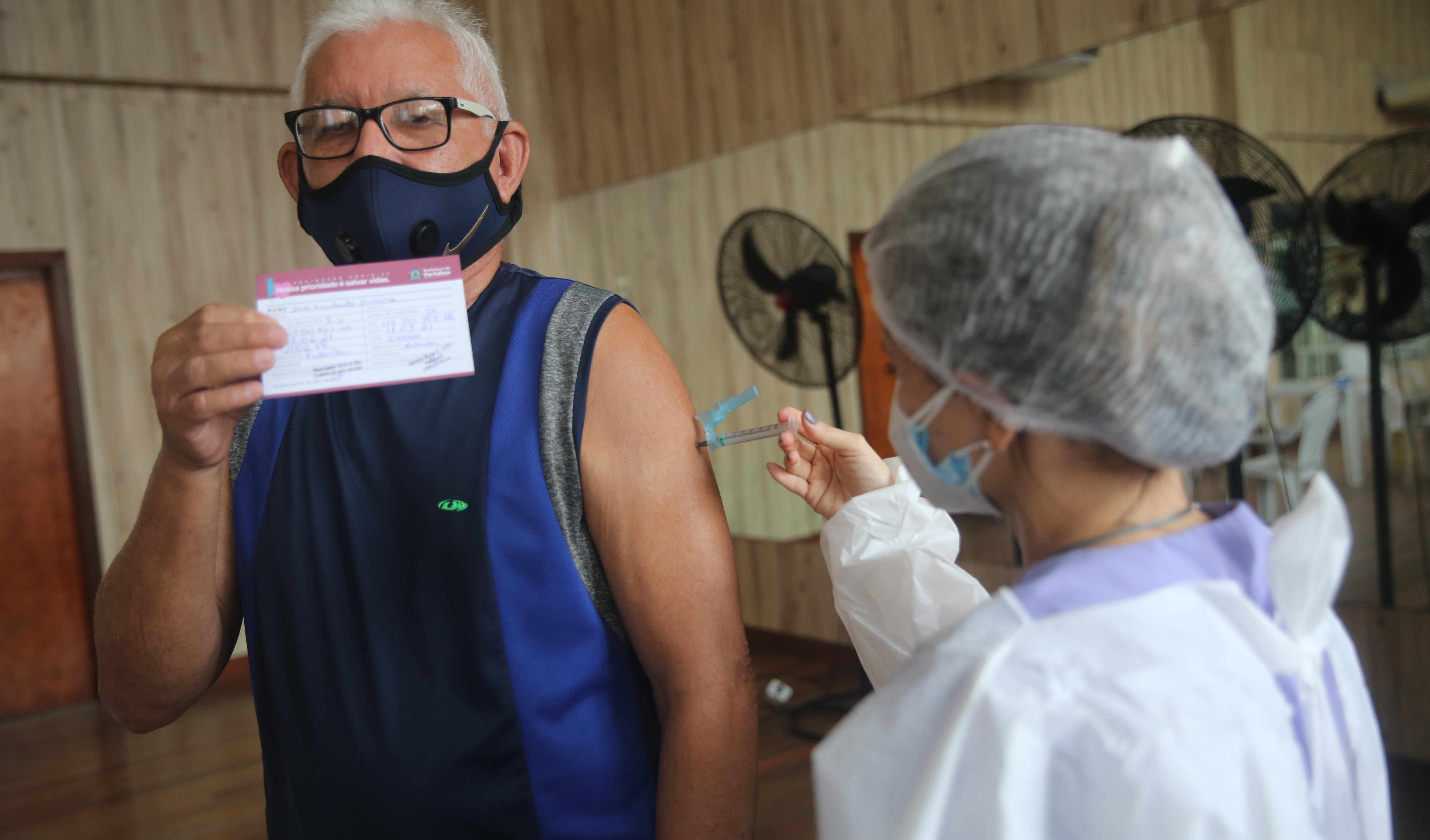 senhor sendo vacinado e mostrando seu cartão de vacinação para a câmera